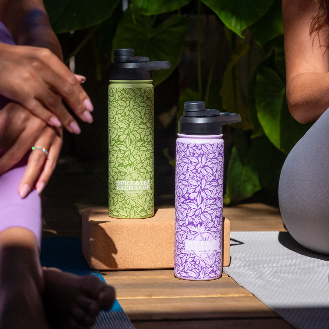 Two insulated water bottles, one green and one purple, on a wooden surface with people sitting around.